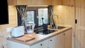 A compact kitchen with wooden cabinets, a built-in stove, a sink, and a window with curtains. - Sugar Hut by Tiny Away (Great Horkesley)