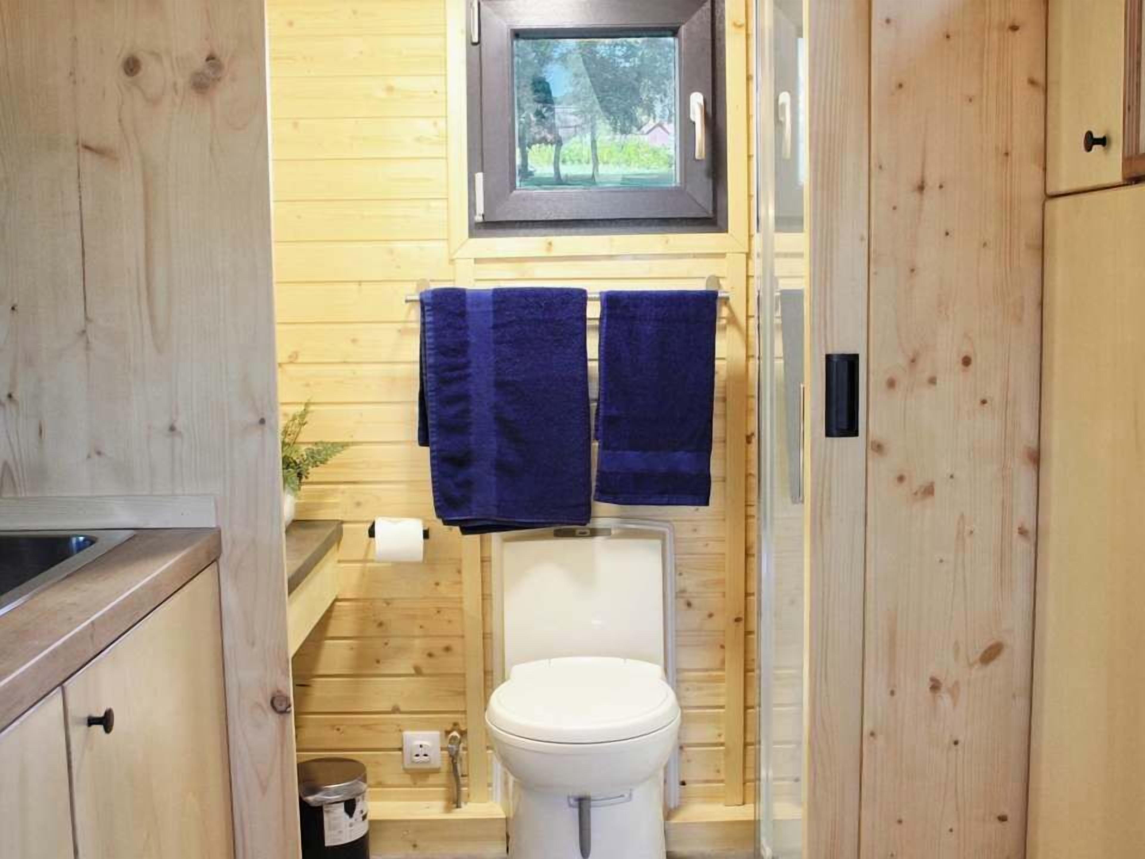 Une petite salle de bain en bois comprenant des toilettes, deux serviettes, une fenêtre et un lavabo.