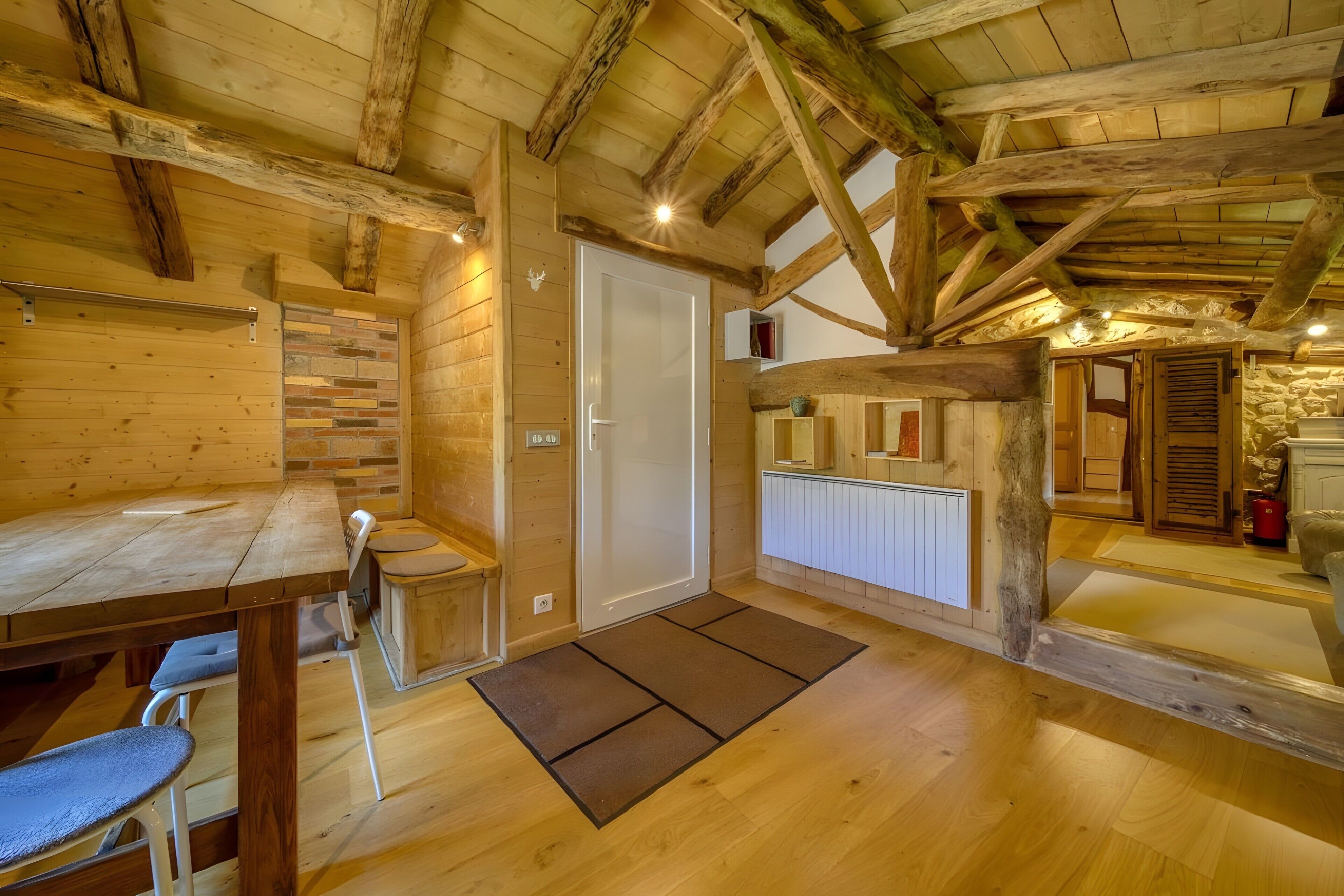 A rustic wooden interior with a wooden table, chairs, a door, and a small kitchen area.
