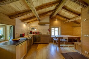 A rustic kitchen with wooden beams, a dining area with a table and chairs, and a window providing natural light. - Holiday Home L'Echappée En Vercors – Astronomy, Hiking, Nature & Relaxation (Choranche)