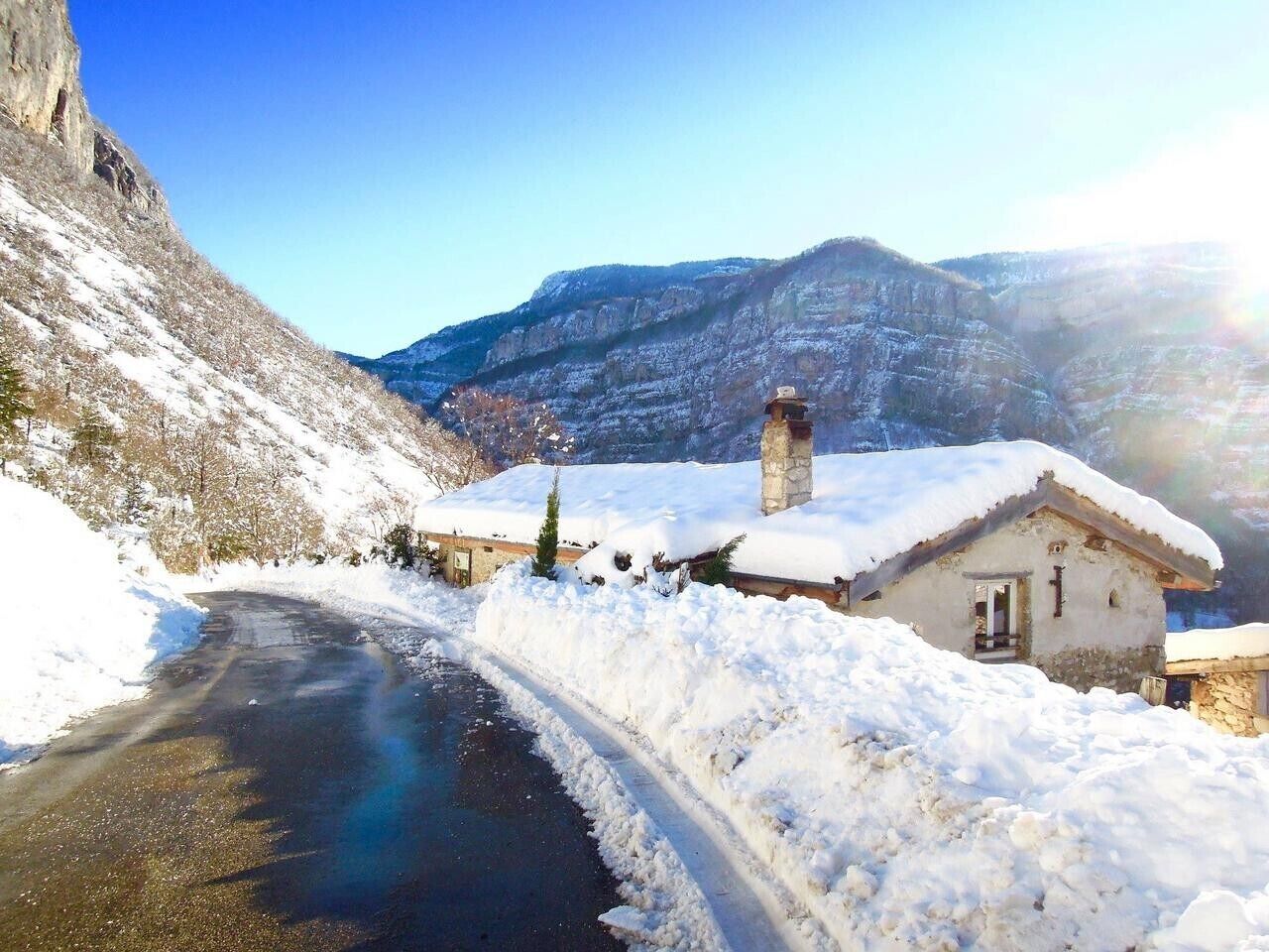 A snow-covered rural road with a house and a mountain in the background.