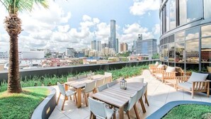 A rooftop terrace with outdoor seating, a palm tree, and a city skyline view.