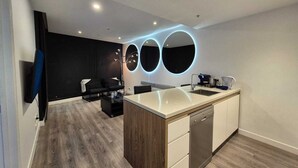 A modern kitchen with a central island, built-in dishwasher, and a dining area with a black sofa and a coffee machine.