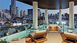 A rooftop pool area with lounge chairs and a view of the city skyline.