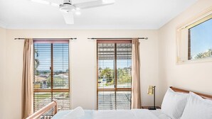 A hotel room with a bed, a ceiling fan, two windows with curtains, a nightstand with a lamp, and a view of the outside. - Peaceful 4B2B Sweet Home w/Backyard @ Springfield (Springfield)