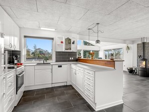 Une cuisine moderne avec des meubles blancs, un îlot central, une cuisinière intégrée et une grande fenêtre offrant une vue sur l’extérieur.