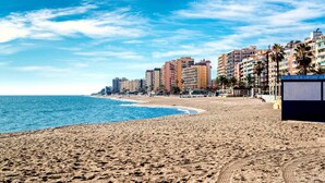 A beach with a sandy shore, a clear blue sky, and a row of multi-story buildings in the background.