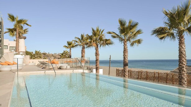 Une piscine à l’eau d’un bleu cristallin, entourée de palmiers et offrant une vue sur l’océan.