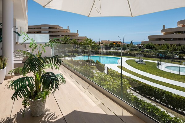 A balcony with a view of a swimming pool, palm trees, and a clear sky.