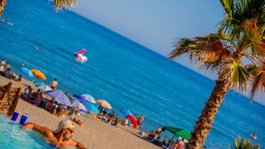 Une scène de plage avec une piscine, des palmiers et des personnes en arrière-plan.