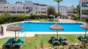 A swimming pool with lounge chairs and umbrellas, surrounded by greenery and buildings. - Miraflores Refurbished by Alfresco Stays (Mijas Costa)