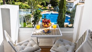 Un balcón con una mesa lista para el desayuno, con vistas a una piscina y vegetación.