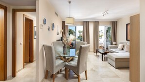 Una sala moderna con una mesa de comedor de vidrio, sillas tapizadas en gris, un sofá color beige y vistas al exterior.