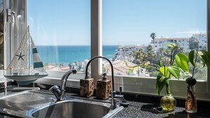 Una cocina con un lavamanos, una decoración de velero y vistas al océano y edificios.