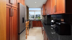 Una cocina moderna con armarios de madera, un refrigerador de acero inoxidable, una cafetera y vistas al exterior a través de grandes ventanas.
