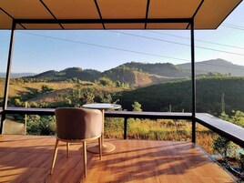 Un balcon donnant sur des collines verdoyantes, avec une table et une chaise.