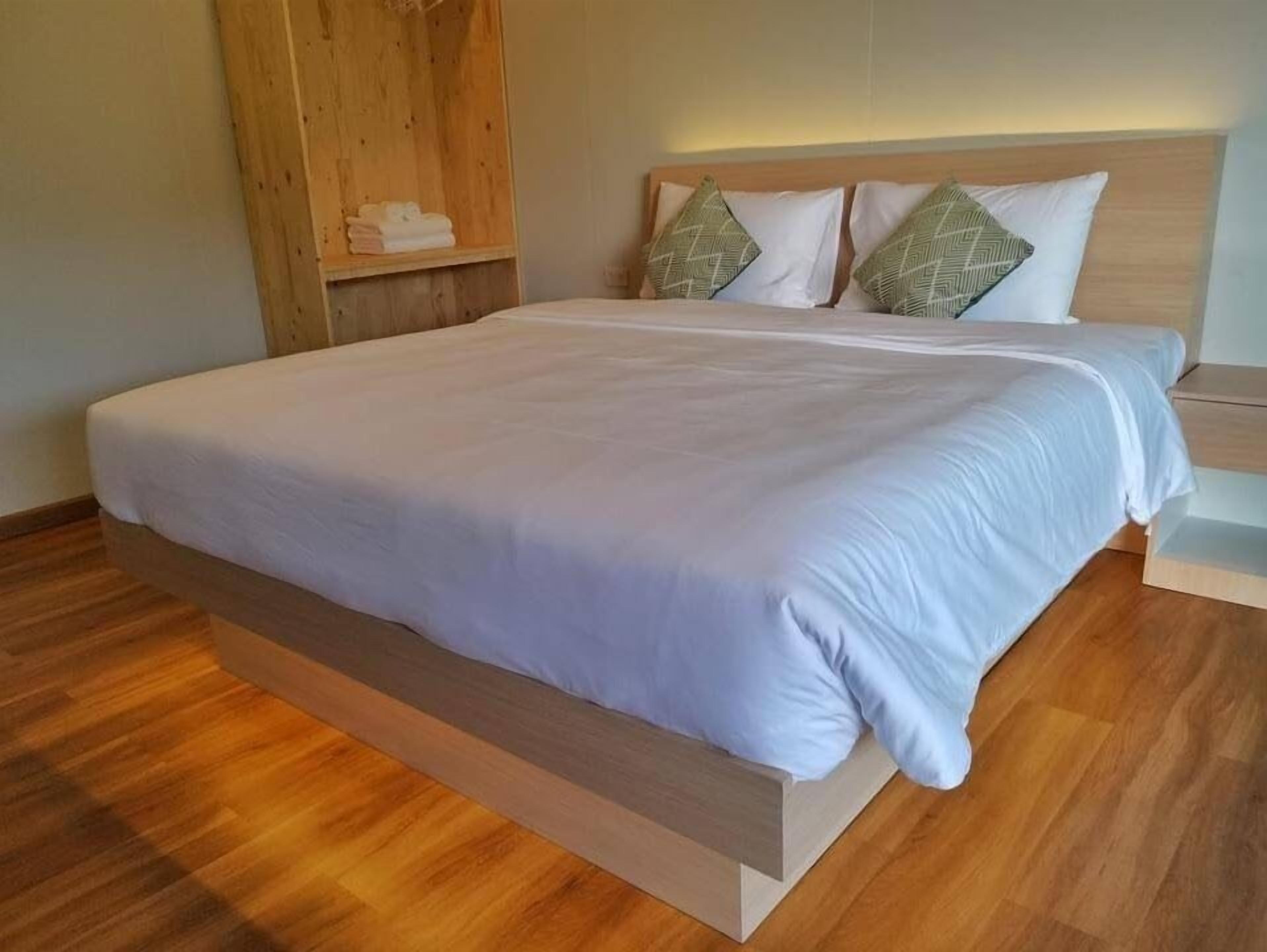 Une chambre moderne avec une tête de lit en bois, un grand lit recouvert de linge de maison blanc et un plancher en bois.