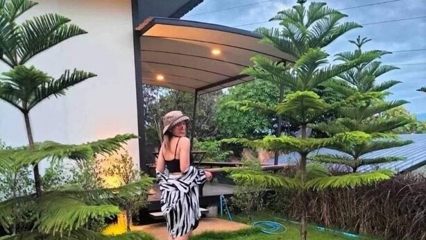 Una casa moderna amb una zona exterior coberta, un jardí i plantes tropicals.