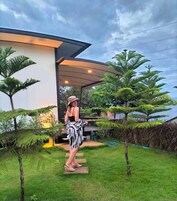 Une maison moderne dotée d’un espace extérieur couvert, d’une pelouse et de plantes tropicales.