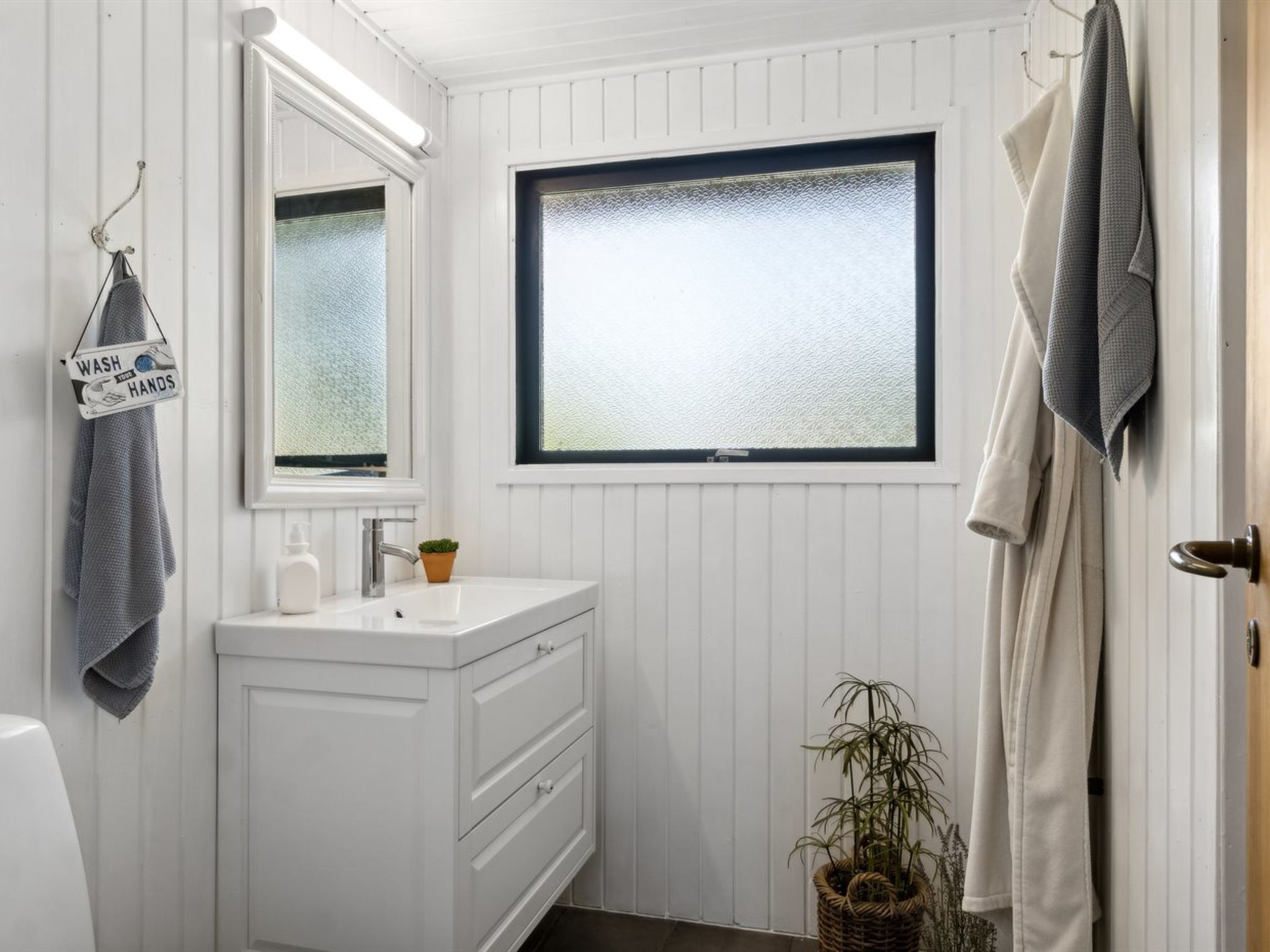 Un baño con tocador blanco, espejo, ventana y toallero.