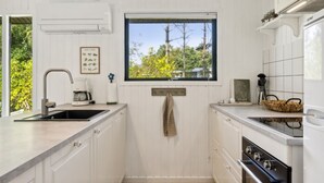 A compact kitchen with white cabinetry, a window with a view of trees, a coffee maker, and a stove. - "Lavrans" - 1km from the sea by Interhome (Ebeltoft)