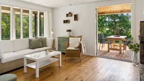 A modern living room with a sofa, coffee table, and wicker chair. A wooden deck is visible through the glass door. - "Lavrans" - 1km from the sea by Interhome (Ebeltoft)