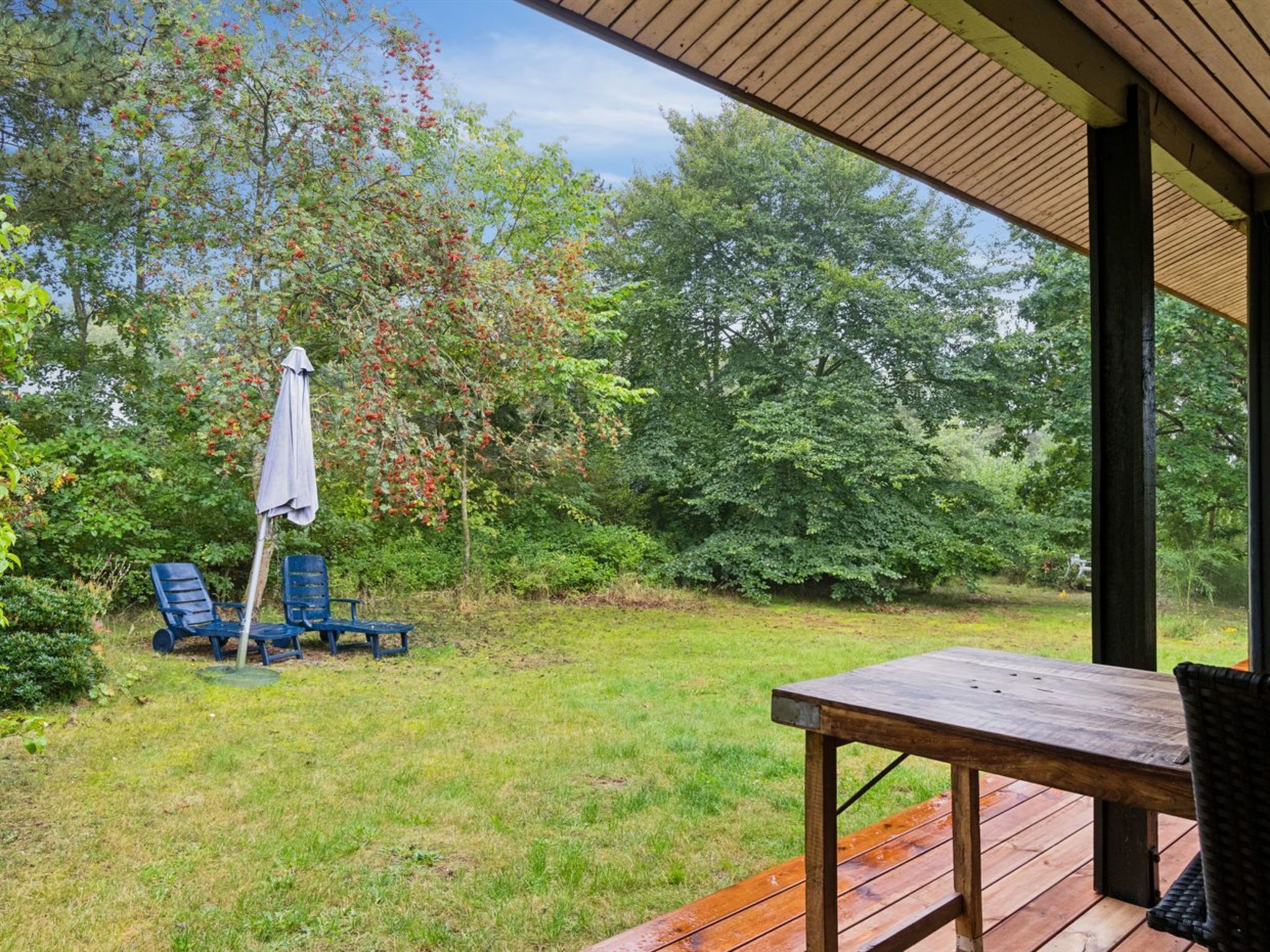 Eine Terrasse im Freien mit einem Holztisch und -stühlen, umgeben von üppiger Vegetation und Bäumen.