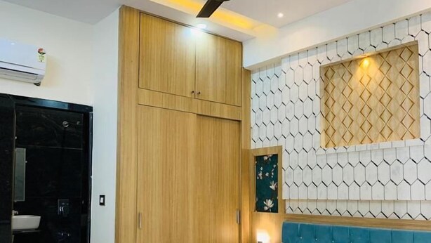 A modern bedroom with a bed, wooden wardrobe, ceiling fan, and a wall-mounted light fixture. - Abhinandan Palace (Udaipur)