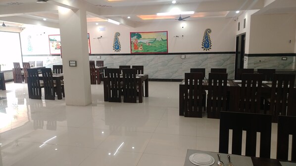 A spacious dining area with marble walls and wooden chairs. - Abhinandan Palace (Udaipur)