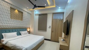 A modern bedroom with a bed, a ceiling fan, a TV, and a wooden door. - Abhinandan Palace (Udaipur)
