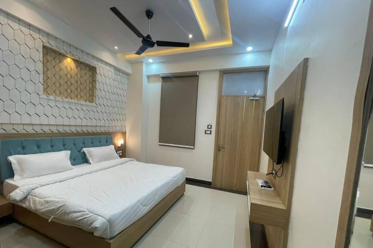 A modern bedroom with a bed, a ceiling fan, a TV, and a wooden door.