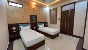 A hotel room with two beds, a wardrobe, a window, and a wall-mounted light fixture. - Abhinandan Palace (Udaipur)
