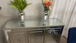 Une console avec un plateau en verre, surmontée de deux vases en argent contenant des plantes et des fleurs.