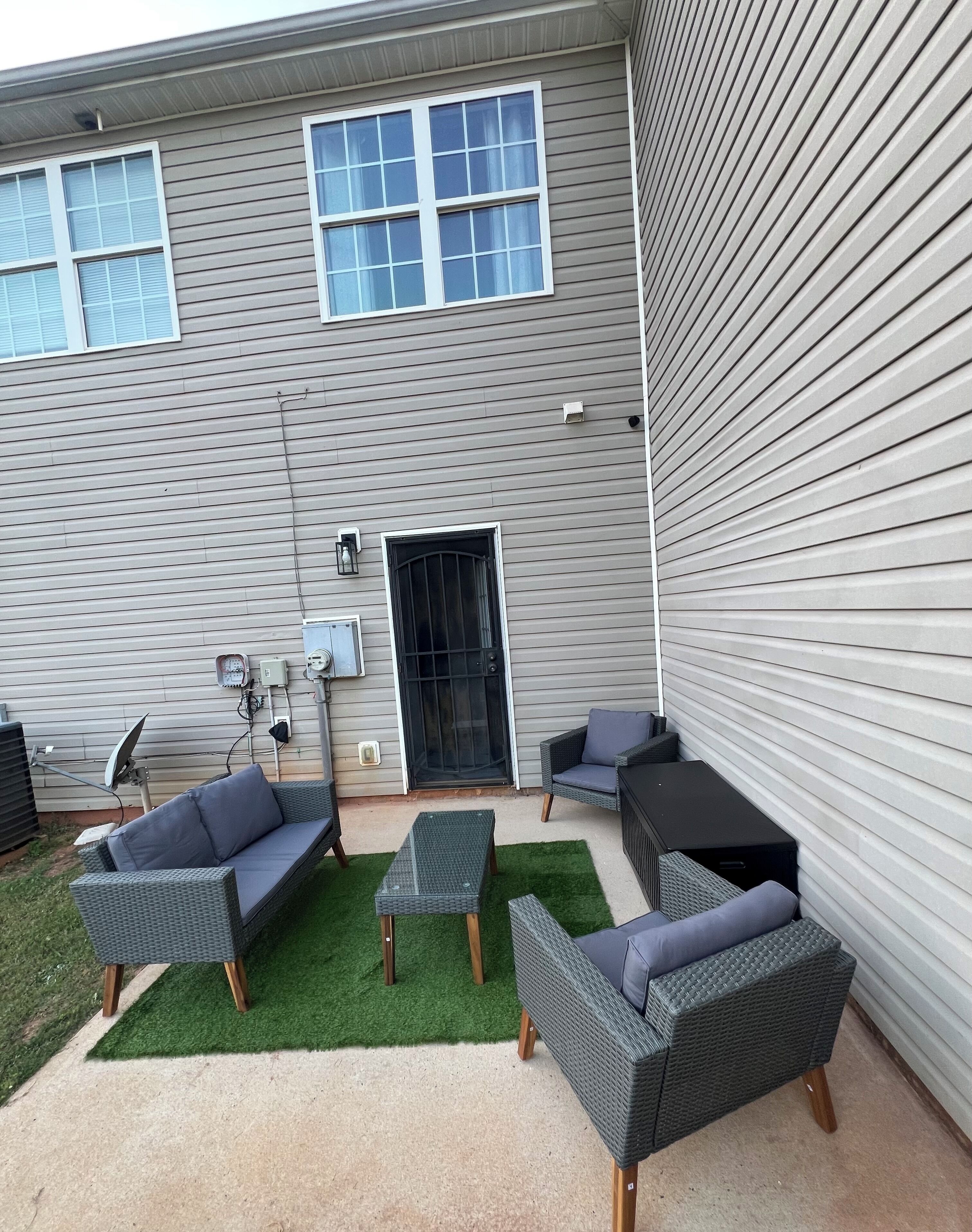 A covered patio area with outdoor furniture, a door, and a wall-mounted air conditioning unit.