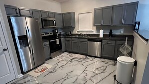 Une cuisine moderne avec des meubles gris, des appareils en acier inoxydable et un sol en marbre.