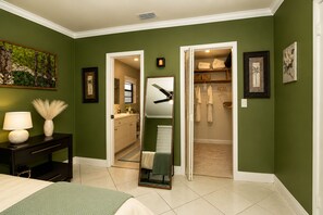 A bedroom with a bed, a nightstand, a lamp, a mirror, and a closet with hanging robes. - House In The Heart of Miami (Miami)