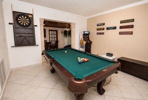 Ein Billardtisch mit Dartscheibe und Billardstöcken, eine Dart-Maschine und eine Wand mit Entfernungsangaben zu verschiedenen Orten.