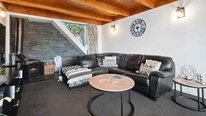 A cozy living room with a stone fireplace, leather sofa, and round coffee tables. - Lakehouse at Panners (Queenstown)