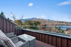 A balcony with wicker furniture overlooking a lake and mountains.