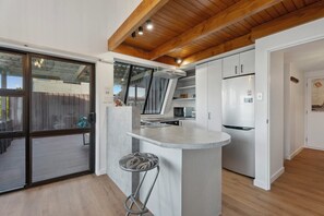 A modern kitchen with a central island, white cabinetry, and a wooden ceiling.
