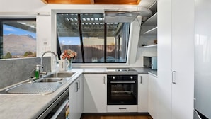 A compact kitchen with a built-in oven, a sink, and a window overlooking a mountainous landscape. - Lakehouse at Panners (Queenstown)