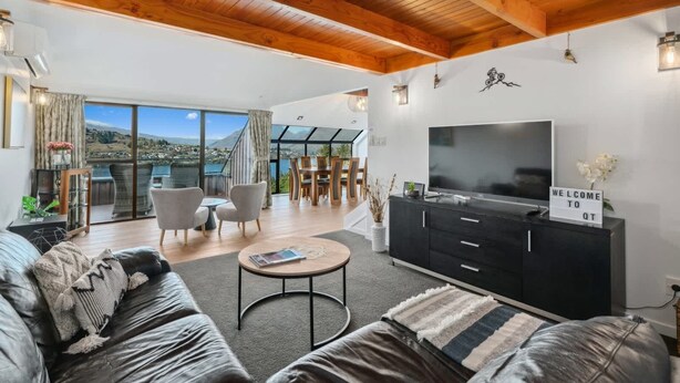 A modern living room with a large TV, black entertainment unit, and a sign reading 'WELCOME TO QT'. - Lakehouse at Panners (Queenstown)