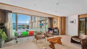 A modern living room with a large glass door leading to a balcony, a wooden coffee table, and leopard print furniture. - Lakeview Park Apartment (Wanaka)