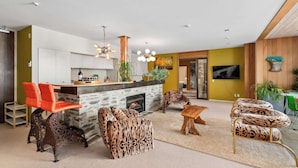A modern living room with a fireplace, leopard-print furniture, and a kitchen area with a white countertop and red chairs. - Lakeview Park Apartment (Wanaka)