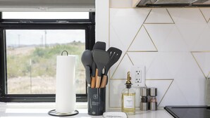 A kitchen counter with a paper towel holder, a spice rack, a bottle of oil, and a digital scale. - Stardust Big Bend Container Home (Terlingua)