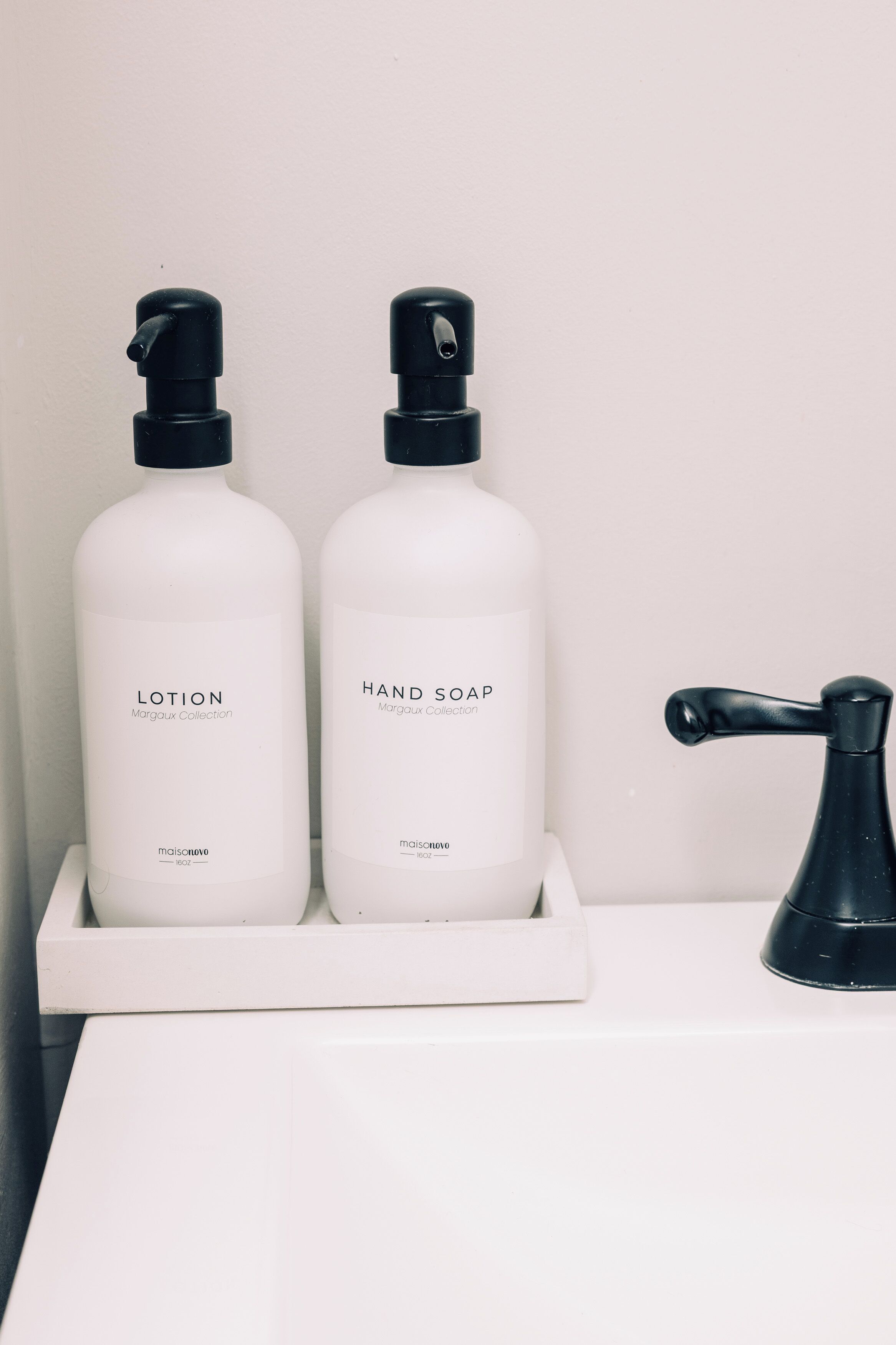 Two white bottles labeled 'LOTION' and 'HAND SOAP' from the Margaux Collection on a white tray.