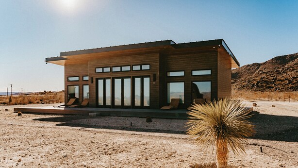 A modern building with large windows and a flat roof, situated in a desert landscape with sparse vegetation. - Stardust Big Bend Container Home (Terlingua)