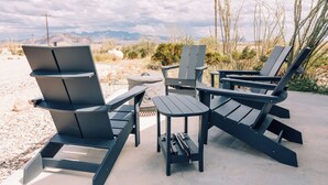 Outdoor furniture including chairs and a table, set on a concrete surface with a desert landscape and mountains in the background. - Stardust Big Bend Container Home (Terlingua)