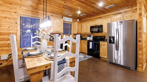 A wooden interior with a dining table, chairs, a refrigerator, a microwave, and wooden cabinets.