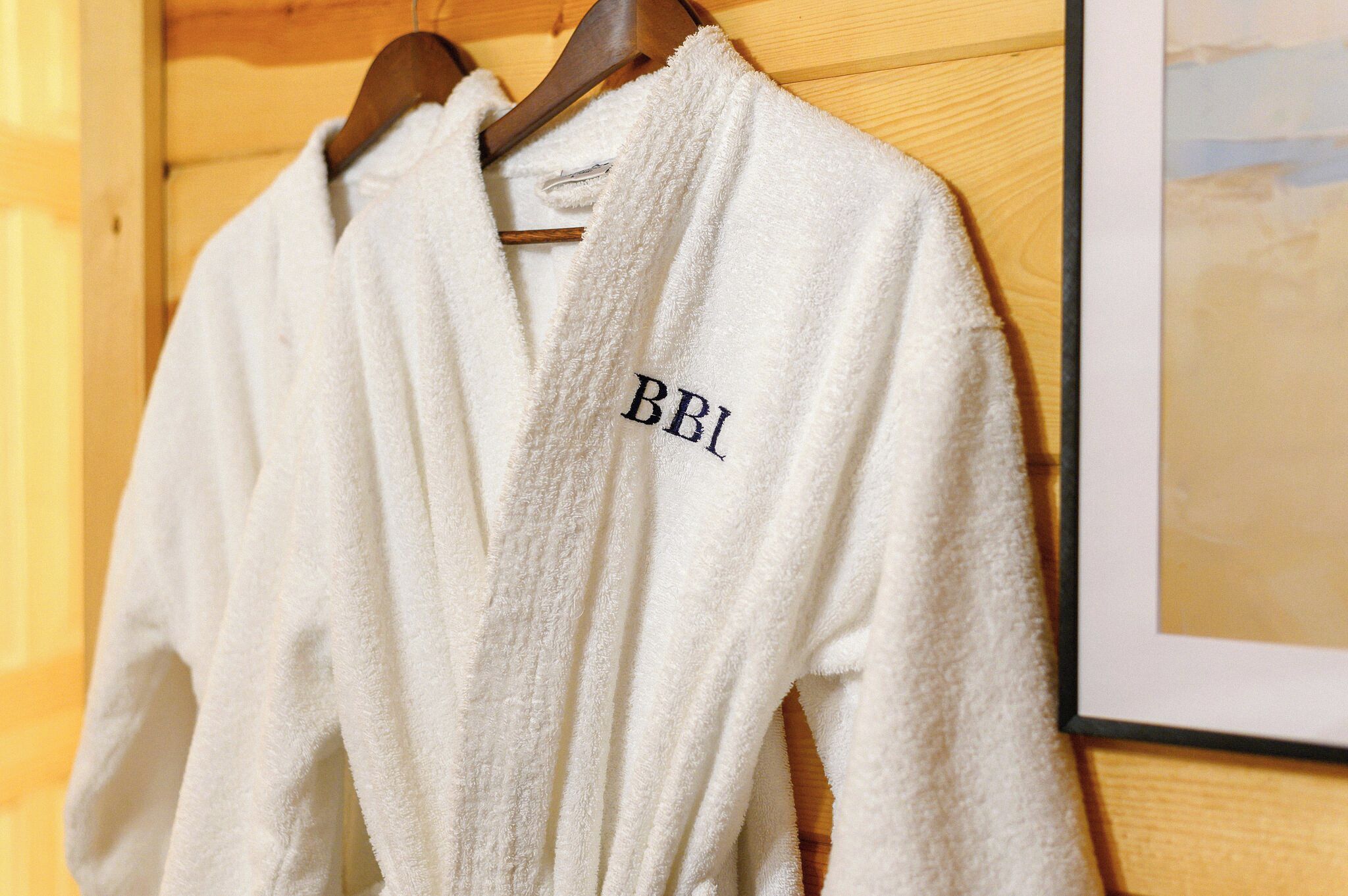 Un peignoir blanc avec les lettres « BBI » brodées, suspendu à un cintre en bois.